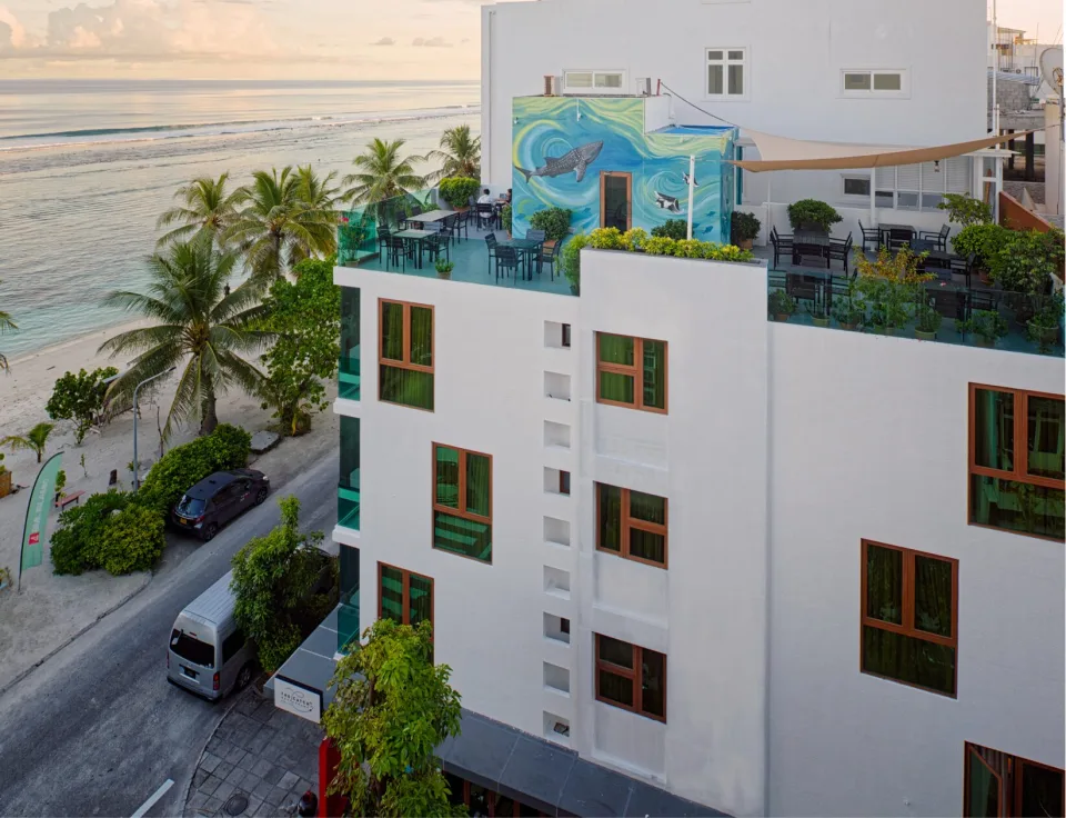 Edifício do h78 junto à praia de Hulhumalé, com terraço e palmeiras à beira-mar